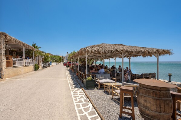 A seaside restaurant with outdoor seating, a stone pathway, and a view of the sea. - Petrina Villa 3 (Viannos)
