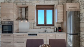 A modern kitchen with light wood cabinets, a stainless steel refrigerator, a built-in oven, and a window above the sink. - Petrina Villa 3 (Viannos)