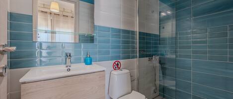 Un baño con un lavamanos blanco, un espejo, un inodoro y una ducha.