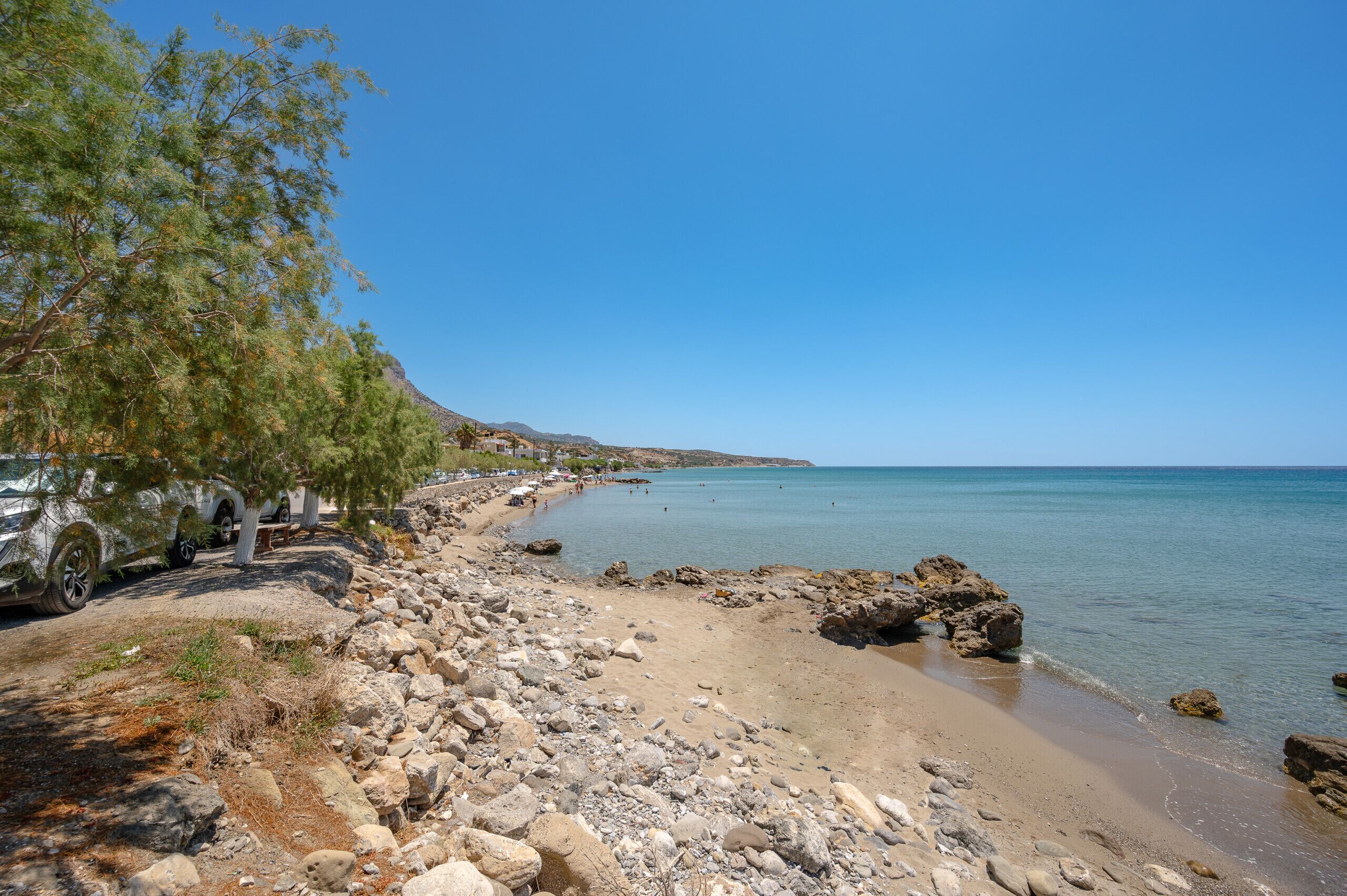 Ein felsiger Strand mit geparkten Autos und blauem Himmel.