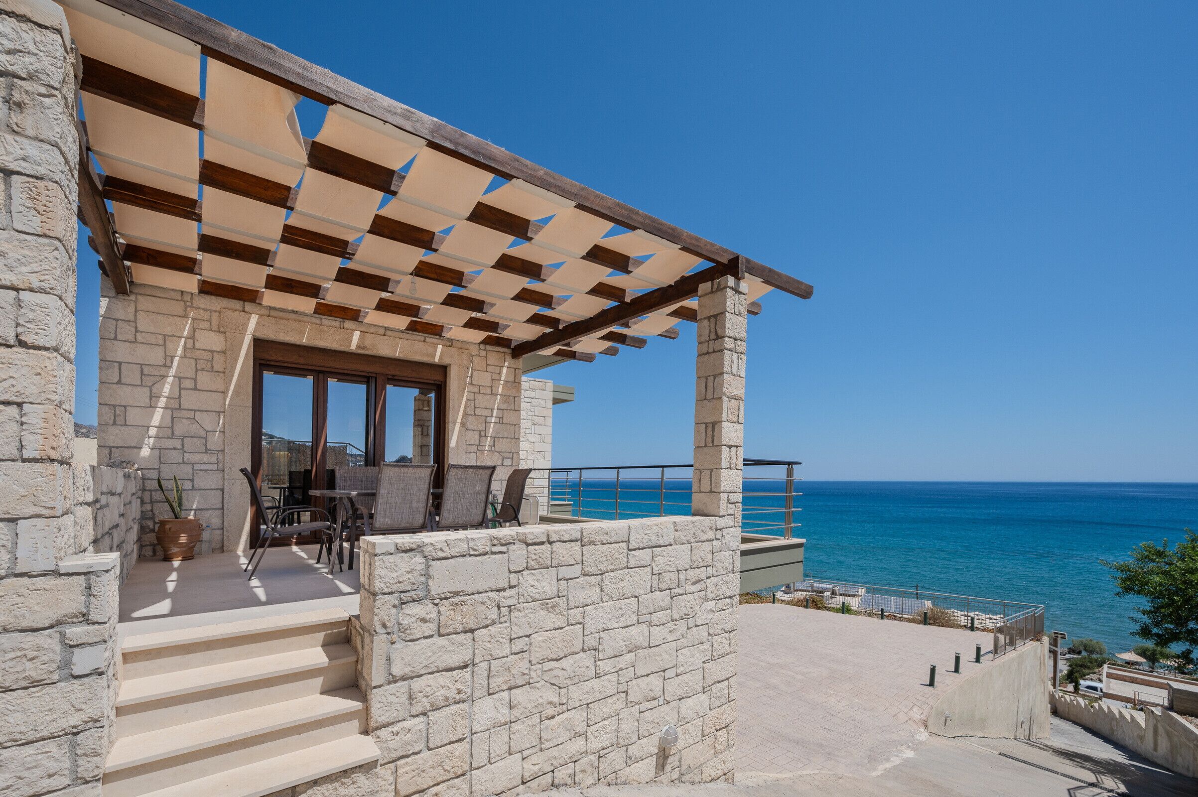 A stone building with a pergola, outdoor seating, and a view of the sea.