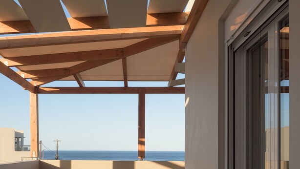 Un balcon avec vue sur la mer, des poutres en bois, une table avec des oranges et deux chaises.