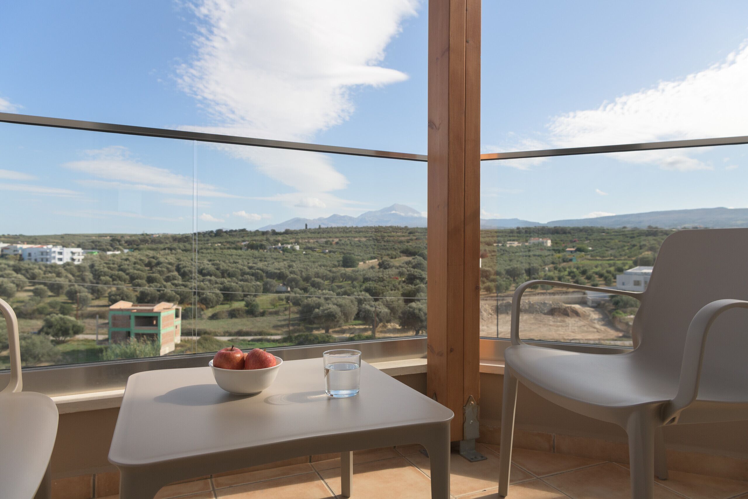 A balcony with a table, a chair, a bowl of fruit, and a glass of water.