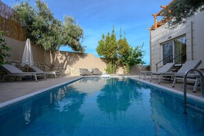 A swimming pool with lounge chairs and a stone wall. - Foothills Tangerine Villa (Rethymno)