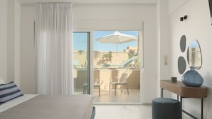 A hotel room with a bed, a small table, a chair, a balcony with an umbrella, and a view of the outside.