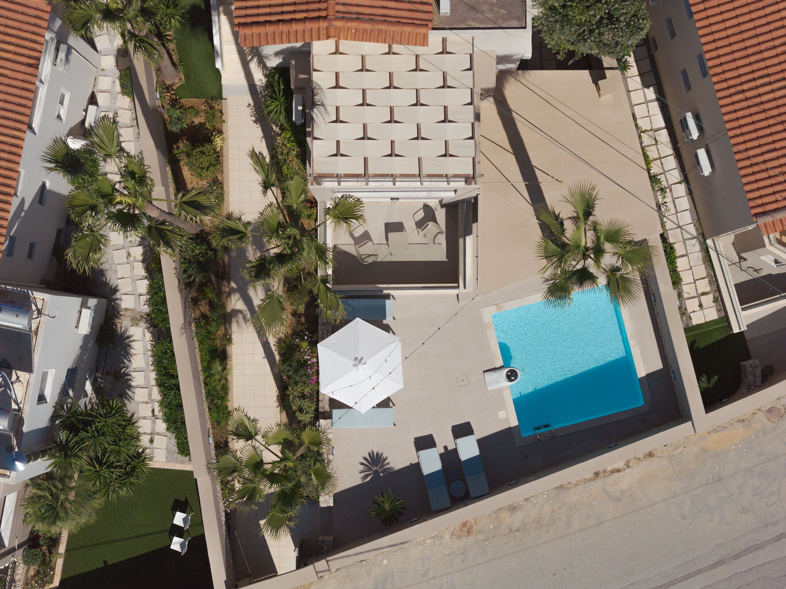 Luchtbeeld van een woonhuis met zwembad, buitenmeubilair en palmbomen.