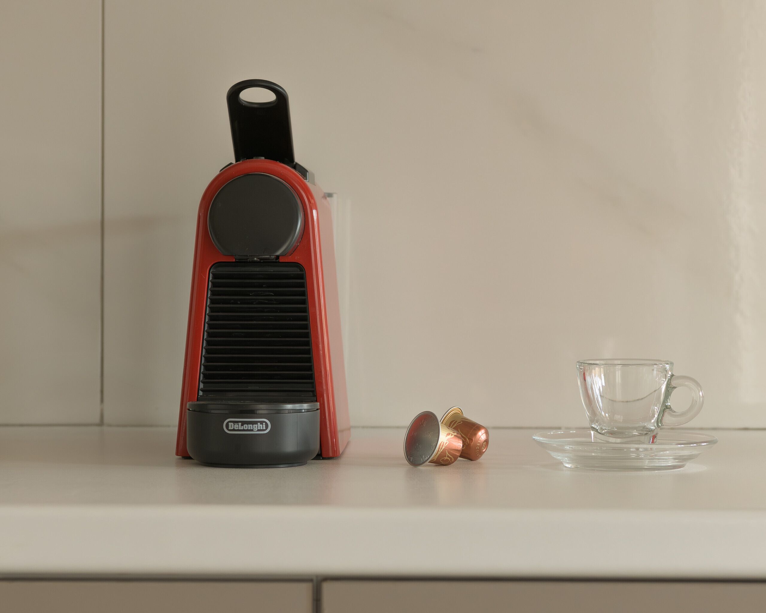 Una cafetera, una taza de vidrio y un platillo sobre una encimera de cocina.
