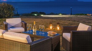 An outdoor dining area with wicker furniture, a table set with wine glasses and a bottle, and lanterns. - Artemis beachfront Villa (Hersonissos)