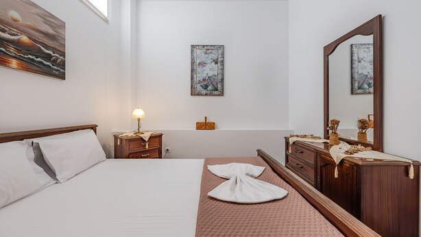 A hotel room with a bed, a nightstand, a dresser, a mirror, and two wall-mounted paintings. - Artemis beachfront Villa (Hersonissos)