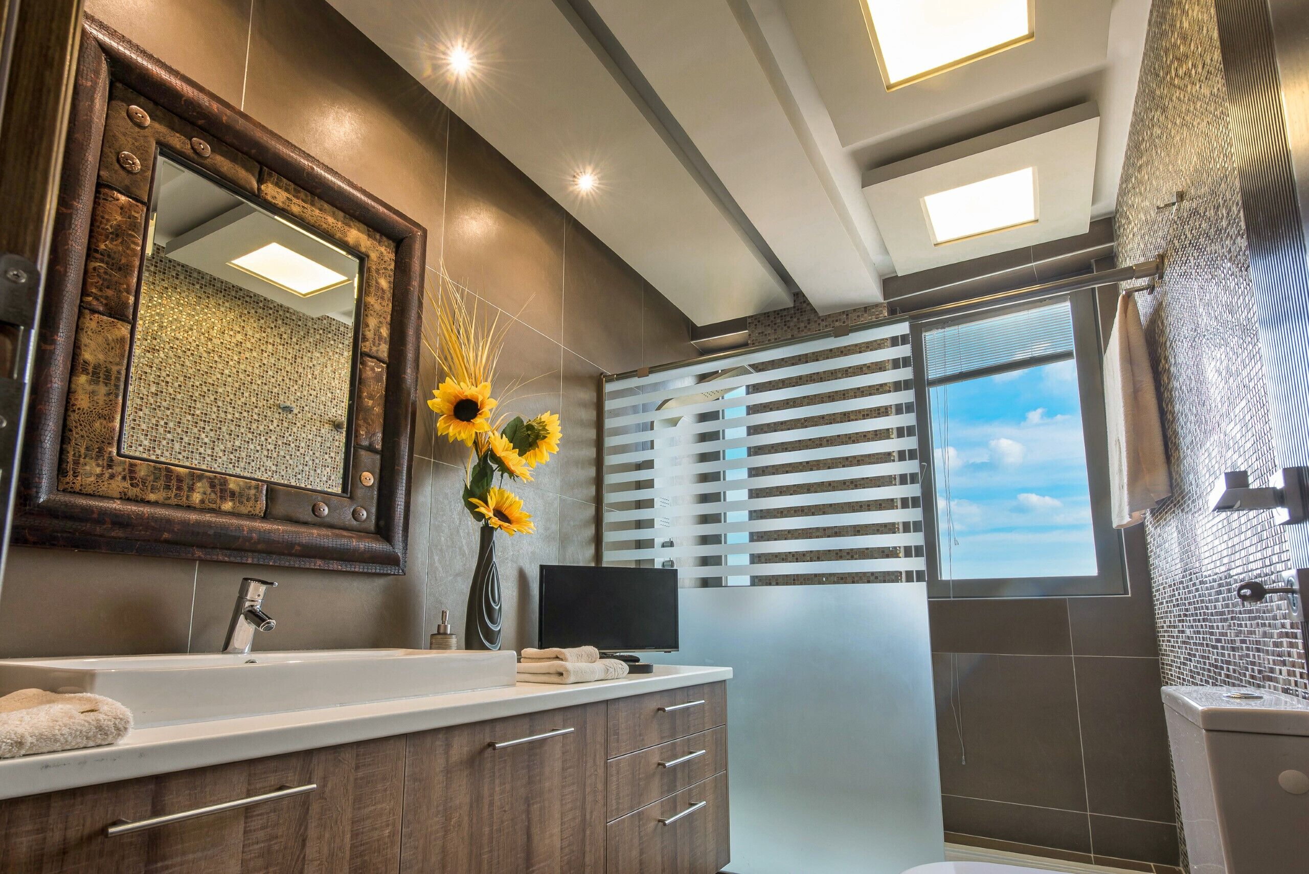 A modern bathroom with a large mirror, a sink with a towel, and a window with blinds.