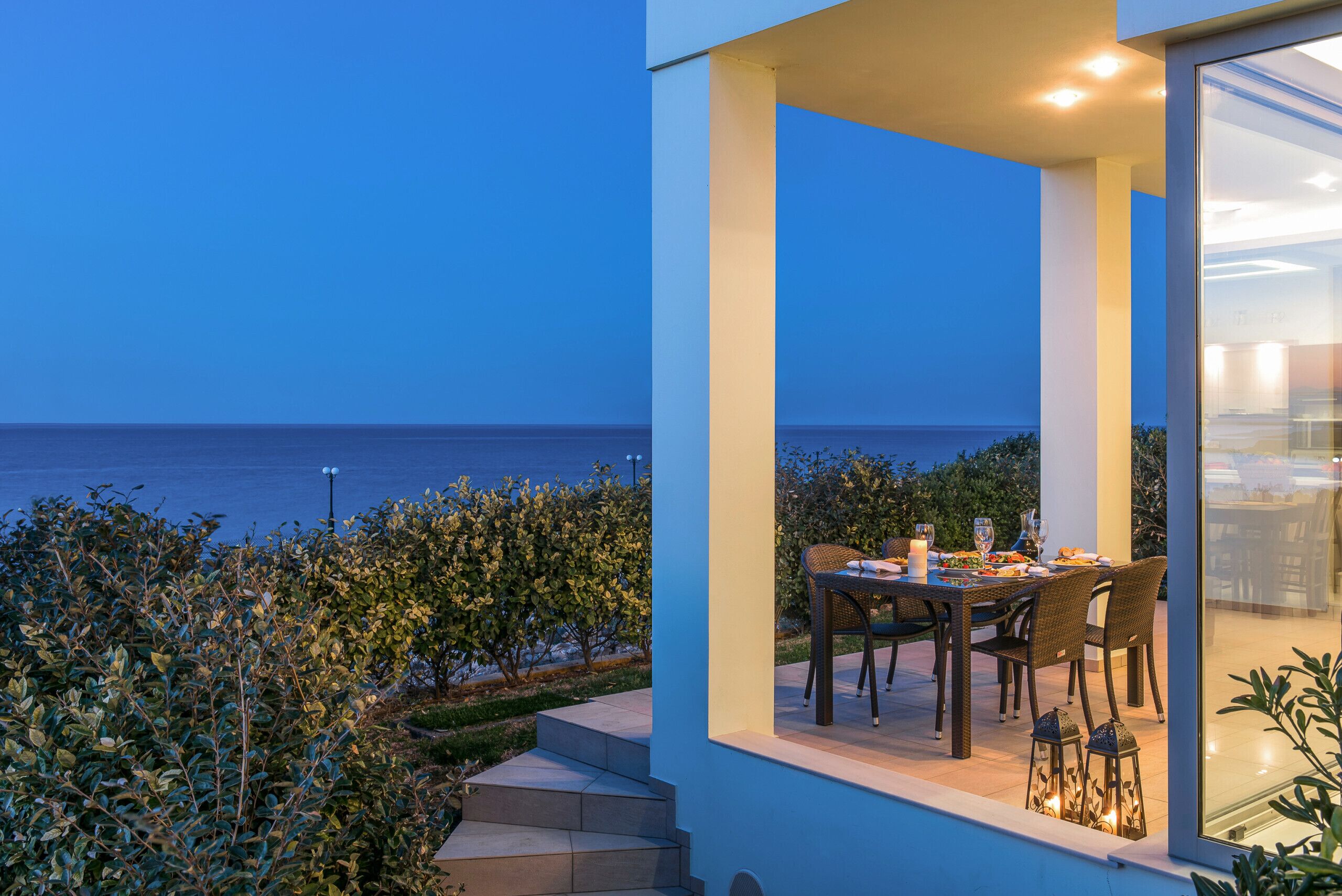 A modern outdoor dining area with a view of the sea, featuring a table and chairs, and a glass railing overlooking the ocean.