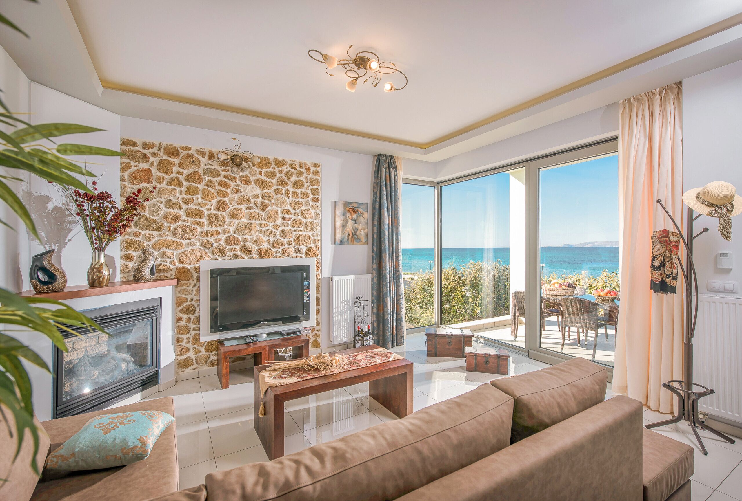 Un salon avec un mur en pierre, une cheminée, un téléviseur et une vue sur la mer.