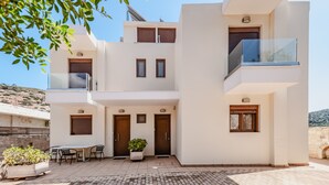 A modern two-story building with a flat roof, a balcony, and a patio area with a table and chairs. - Villa Nikos (Malevizi)