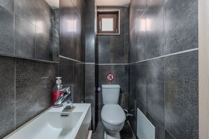 Een moderne badkamer met donkere tegels, toilet, wastafel met zeepdispenser en een rookvrij sign.