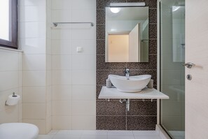 Un baño moderno con un lavabo blanco, una cabina de ducha de vidrio y un espejo sobre el lavabo.