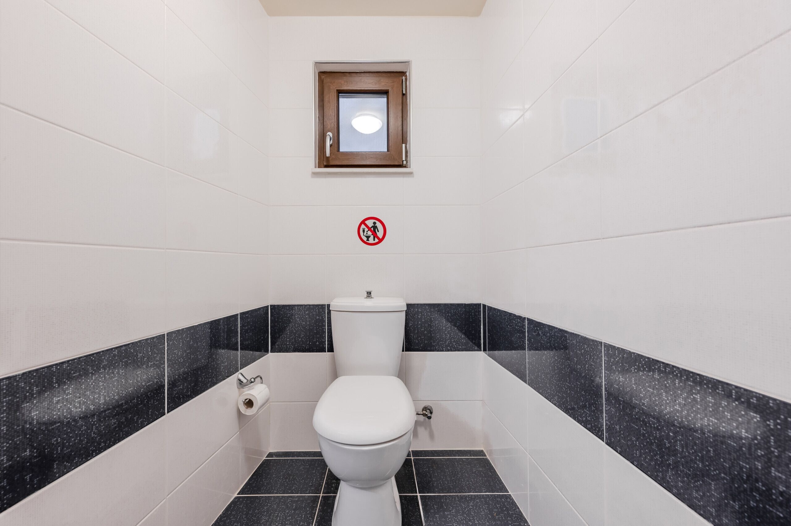 A bathroom with a toilet, a small window, and a no-smoking sign.