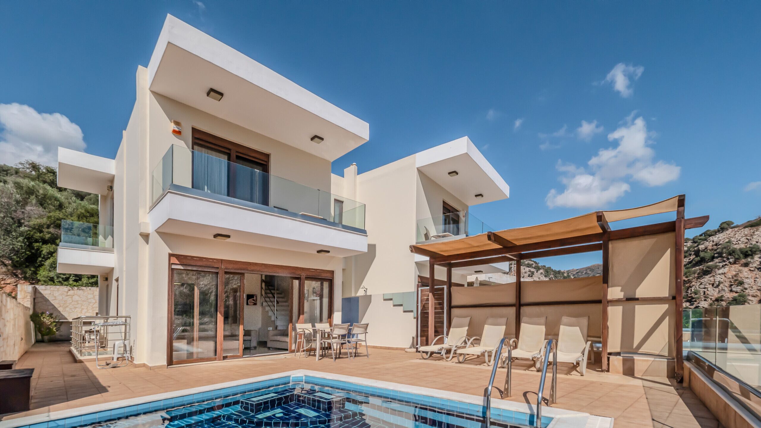 Ein modernes, zweistöckiges Haus mit Swimmingpool, Sitzgelegenheiten im Freien und einer Pergola.