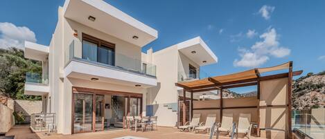 Una casa moderna de dos pisos con piscina, mobiliario exterior y una pérgola.