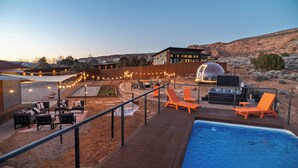 Un espace aménagé au bord de la piscine, avec des chaises longues, un barbecue et des guirlandes lumineuses.