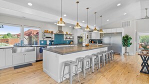 Une cuisine moderne dotée d’un grand îlot central, d’appareils électroménagers en acier inoxydable et de luminaires suspendus.
