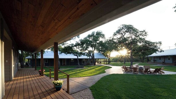 A covered outdoor patio with a wooden deck, a grassy lawn, and a clear view of a house in the background.