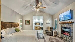 A bedroom with a large bed, a fireplace, a TV, and a ceiling fan.