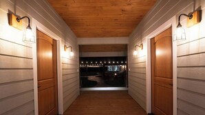 A hallway with wooden doors and light fixtures, leading to a darkened area with string lights.