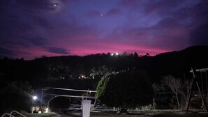 A swimming pool at dusk with a view of a hill and distant lights.
