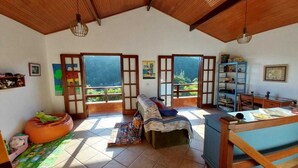 A spacious living room with a high ceiling, a sofa, a wooden table, and a view of the outdoors through large doors.