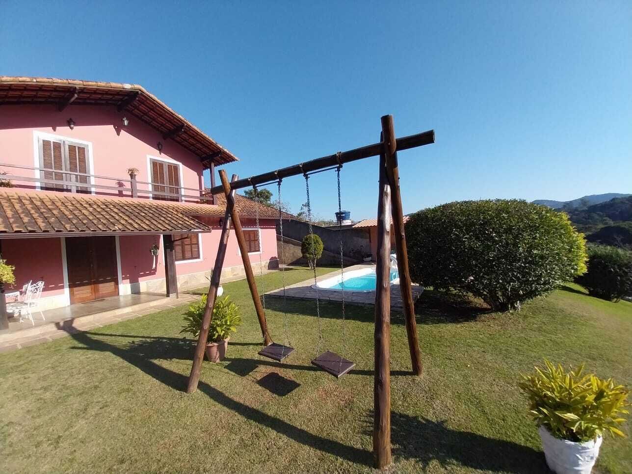 A house with a swimming pool, a swing set, and a well-maintained lawn.