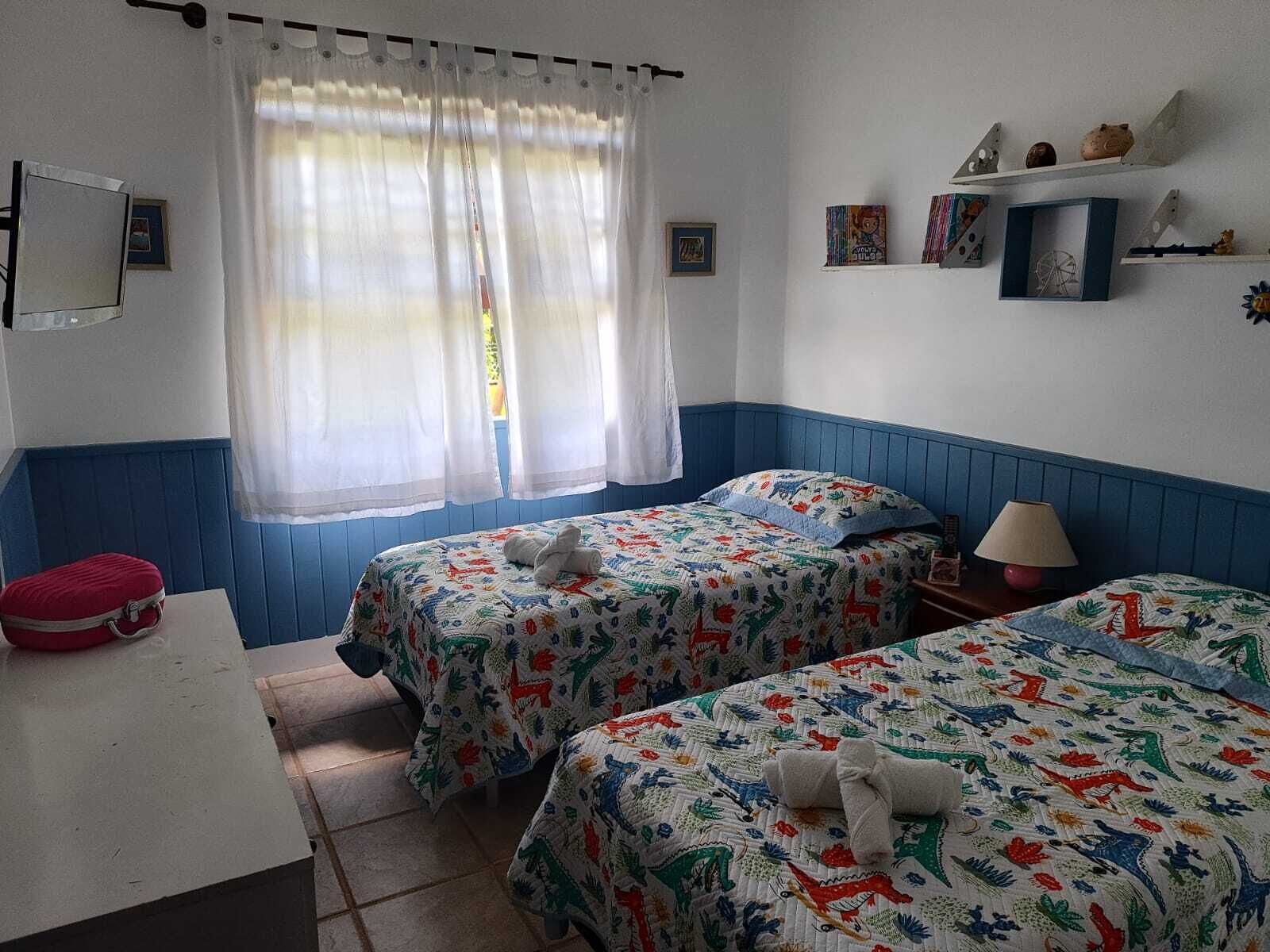 Une chambre avec deux lits, une petite table, une lampe et une étagère ornée d’objets décoratifs.