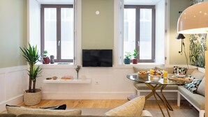 A living room with a sofa, a glass coffee table, a TV, and a window with blinds.