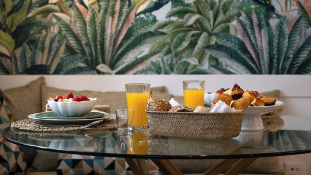 A breakfast setting with a bowl of fruit, two glasses of orange juice, and a basket of pastries on a glass table.