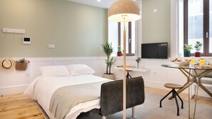A modern bedroom with a bed, bedside table, lamp, and a view of the kitchen area.