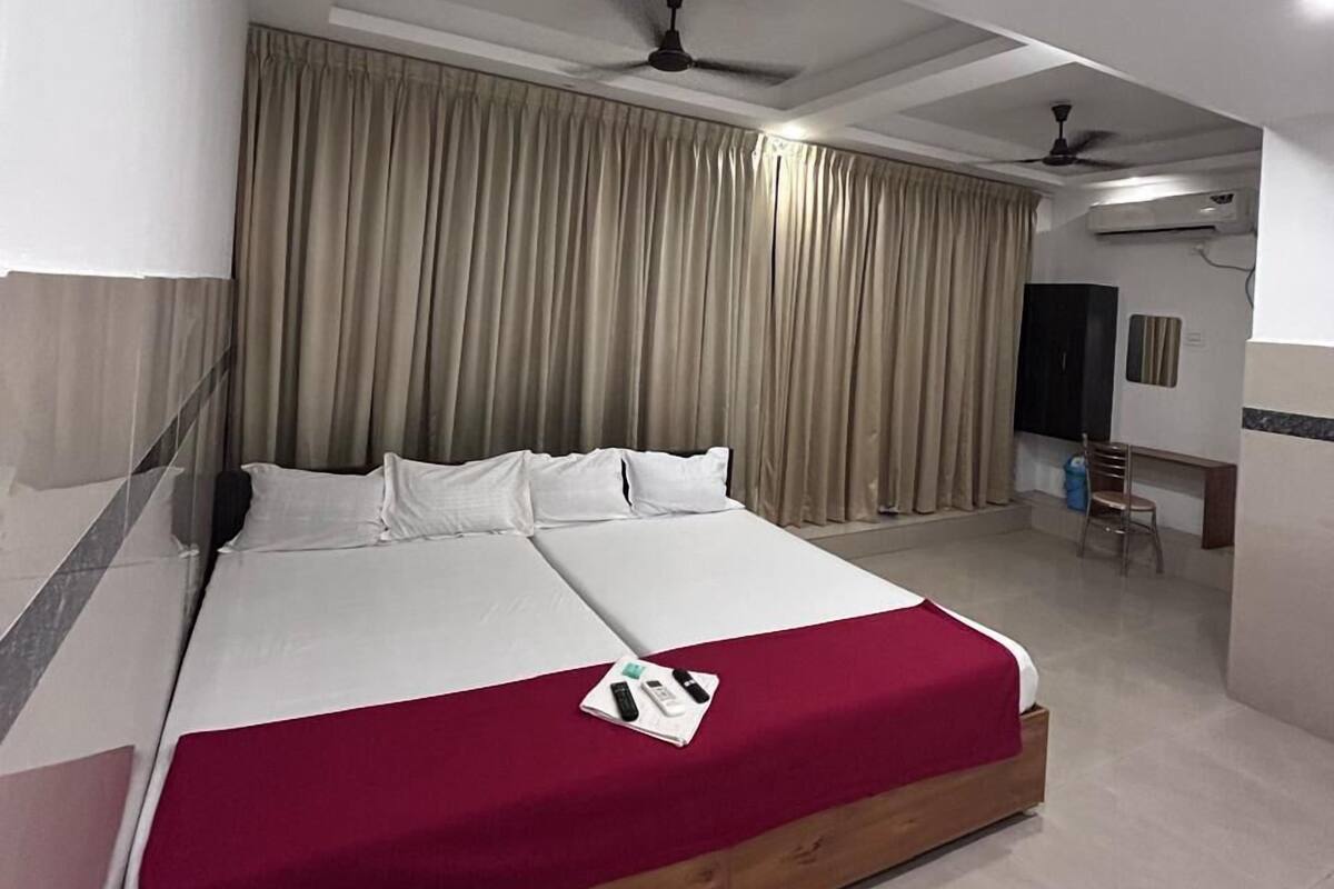 Ein Hotelzimmer mit einem großen Bett, beigen Vorhängen, Deckenventilatoren und einer kleinen Schreibtischzeile.