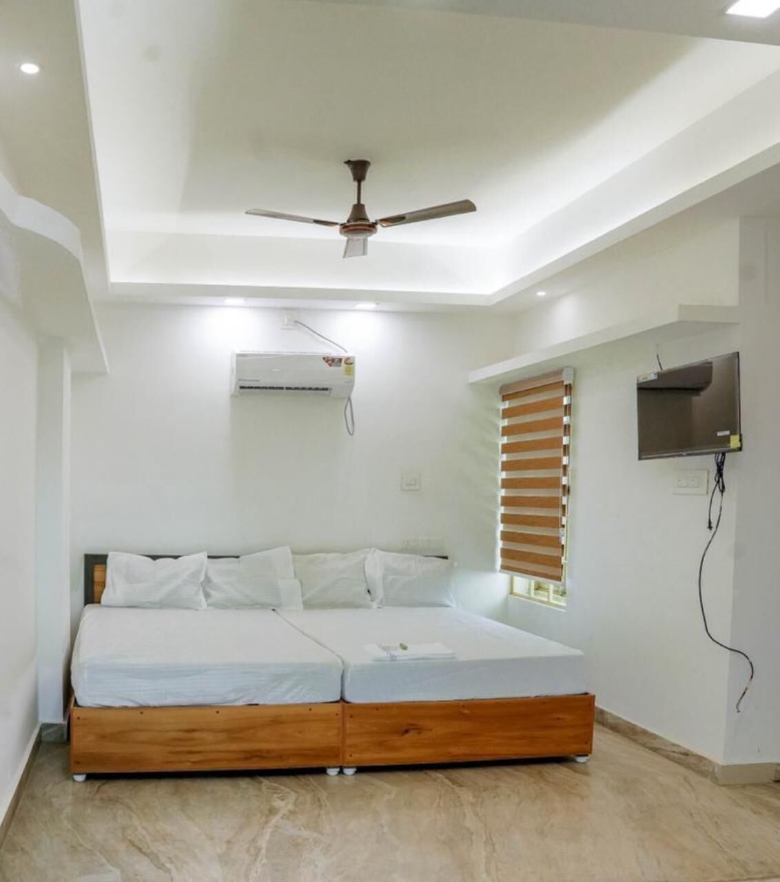 A modern bedroom with a wooden bed, a ceiling fan, an air conditioning unit, a window with blinds, and a mounted television.