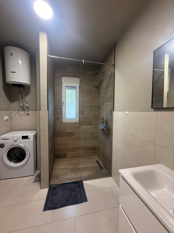 A modern bathroom with a glass-enclosed shower, a built-in washing machine, and a bathtub.