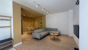 A modern living room with a sectional sofa, a small round table, and a TV mounted on the wall.