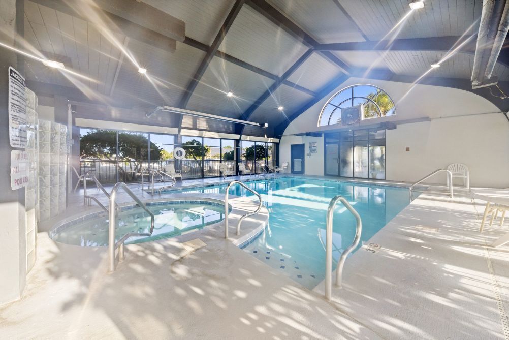An indoor swimming pool with clear glass walls, metal railings, and a high ceiling with skylights.
