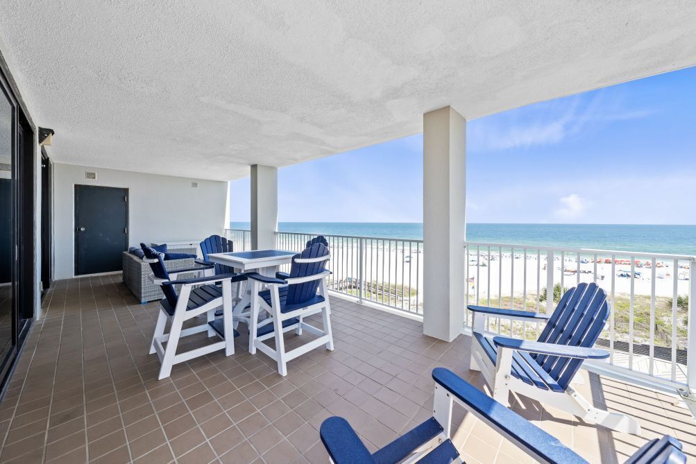 A balcony with a table and chairs, a view of the beach, and a door.