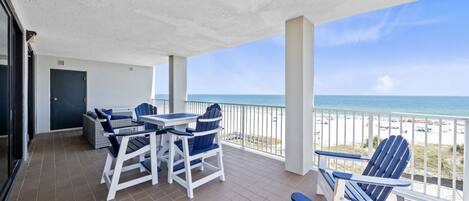 A balcony with a table and chairs, a view of the beach, and a door.