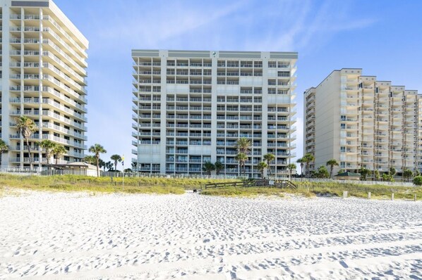 A beachfront hotel with multiple high-rise buildings, a sandy beach, and palm trees. - Pelican Pointe 506 with pools (Orange Beach)
