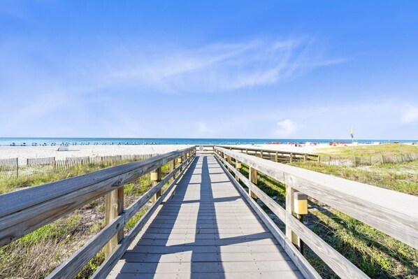 A wooden boardwalk leading to a beach with a clear sky.
