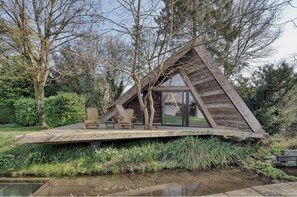 Eine Holzhütte mit geneigtem Dach, einer Terrasse mit zwei Stühlen und einer Glastür zum Eingang.
