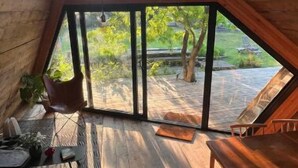A wooden interior with a sloped ceiling, a dining table, a bench, and a view of the outdoors.