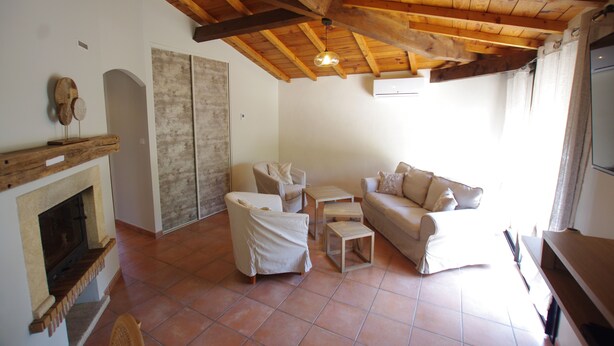 A living room with a fireplace, wooden ceiling beams, a sofa, a chair, and a small table.