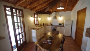 A kitchen with wooden beams, a dining table with chairs, a refrigerator, and a microwave. - Gîtes cosy piscine et spa - Holidays near Bergerac (Bosset)