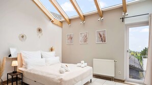 A bedroom with a skylight, a bed, a nightstand, and a radiator.