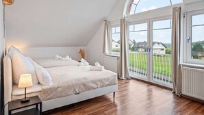 A bedroom with a large bed, a bedside lamp, and a view of a green landscape through large windows.