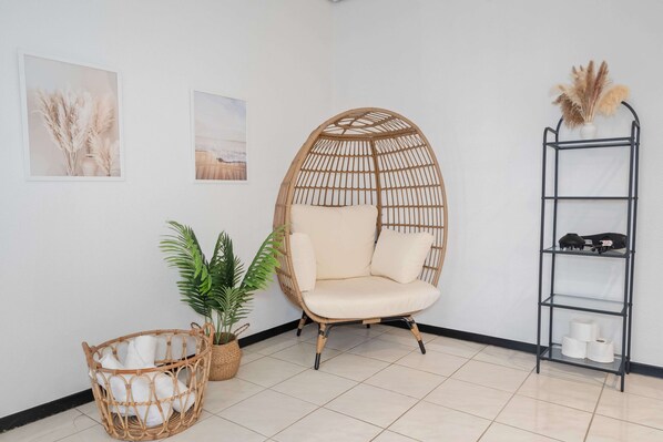 A room with a wicker chair, a wicker basket, a potted plant, and a metal shelf with items.